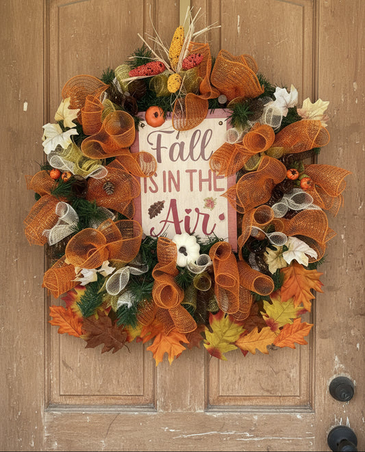 Decorative wreath with 'Fall is in the Air' sign and autumnal ribbons and leaves.